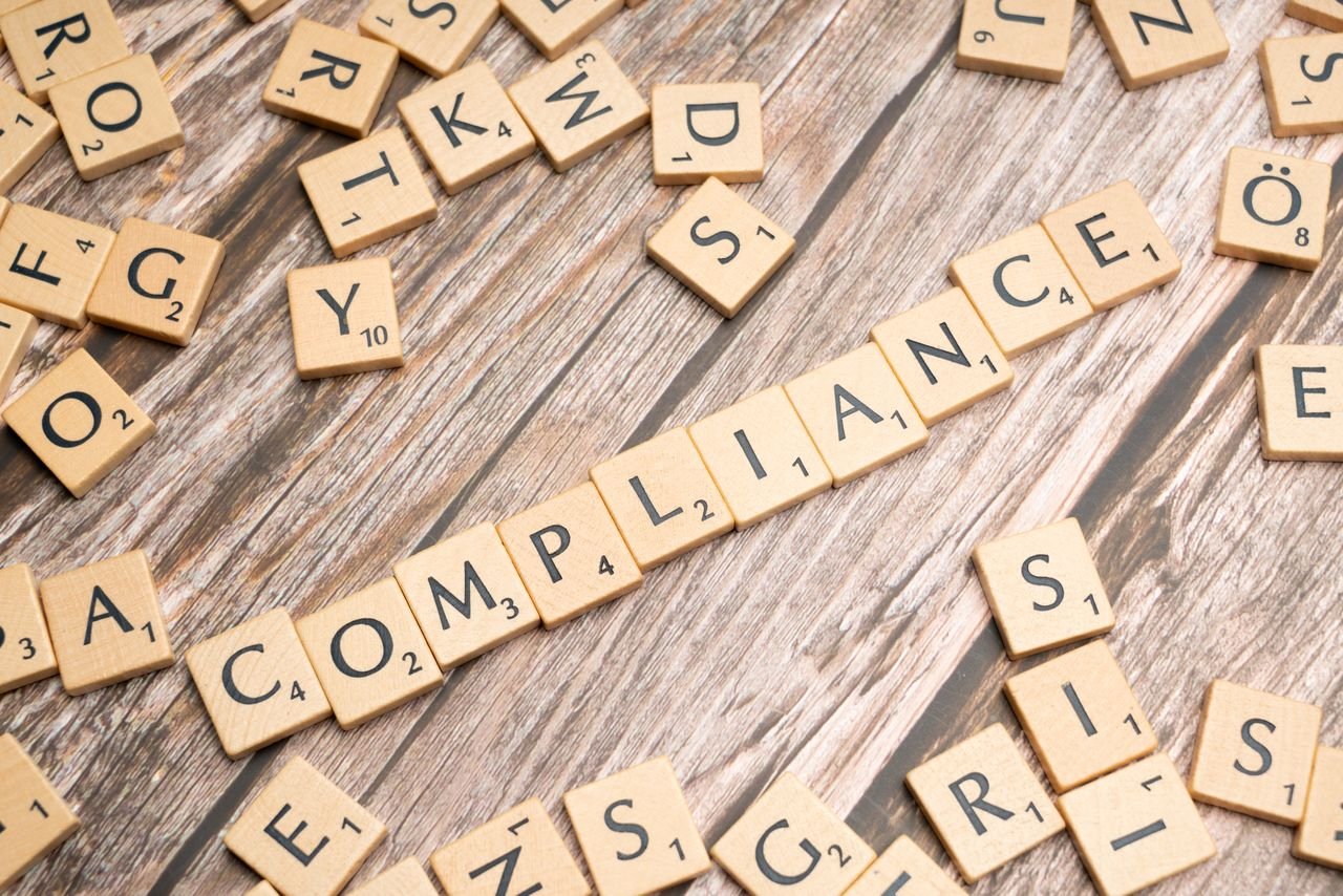 about-01 Wooden letter tiles forming the word 'COMPLIANCE' on a rustic wooden background.