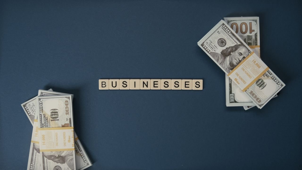 gallery-1 Top view of dollar bills and 'businesses' letter tiles symbolizing financial success.